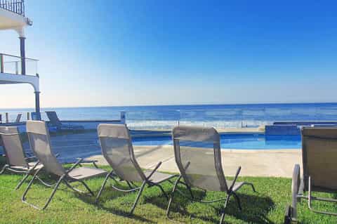 Lounge chairs on grass facing ocean view with pool and beachfront