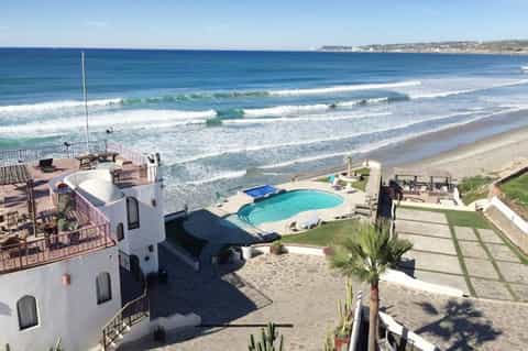 Beachfront property with white building, pool, ocean waves, and cliffside location
