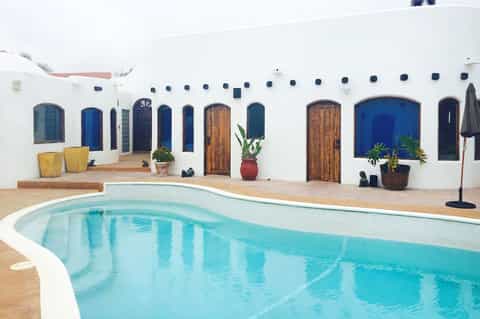 Curved swimming pool in front of white building with blue doors and wooden accents on desert landscape