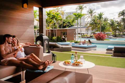 Couple relaxing on terrace overlooking resort pools, palm trees, and ocean views