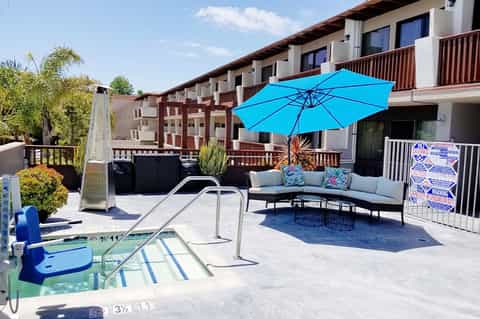 Resort pool deck with blue umbrella, seating area, and multi-story building in background