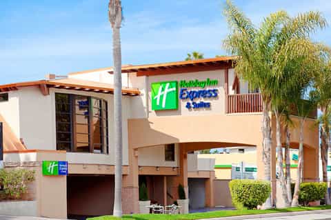 Holiday Inn Express & Suites exterior with orange accents, palm trees, and ground-level entrance