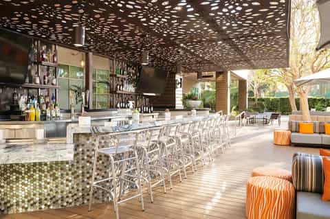 Outdoor bar and lounge with perforated metal ceiling, marble counters, and colorful seating