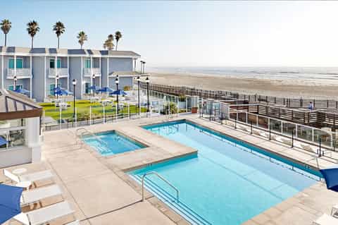 Beachfront pool area with two pools, lounge chairs, and ocean view with white beach cottages