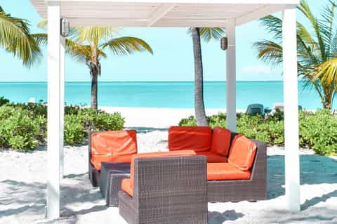 Beachfront lounge area with red cushioned seating, white pergola, and turquoise ocean view