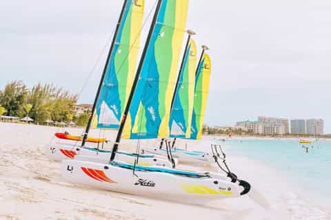Colorful sailboats with blue, yellow and green sails lined up on sandy beach