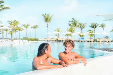 Couple relaxing in resort pool with palm trees and white umbrellas in background