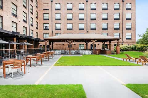 Modern courtyard with green lawn, wooden seating, pavilion, and brick buildings