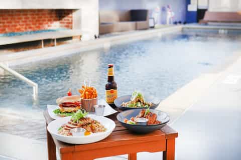 Poolside dining setup with burgers, salad, and beverages overlooking the water