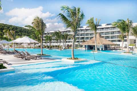 Luxury resort pool with palm trees, loungers, and modern white building architecture