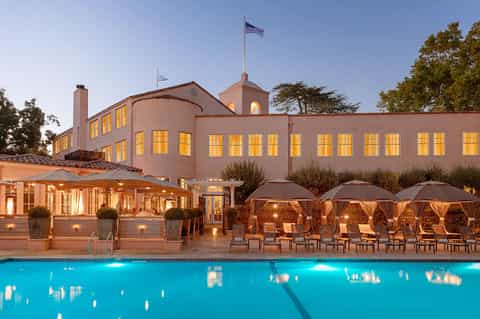 Upscale resort pool at dusk with illuminated building, umbrellas, and lounge seating