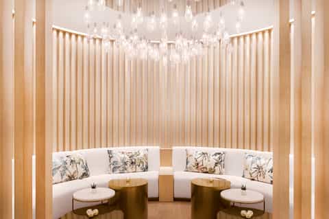 Luxury spa lounge with curved white seating, crystal chandelier, and wooden wall panels