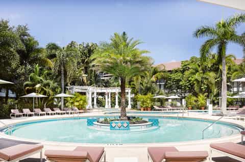 Elegant circular resort pool with palm trees, white umbrellas, and tropical landscaping