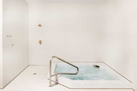 Modern spa hot tub with white tile and metal handrail in minimalist bathroom