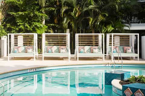 Poolside cabanas with white frames and teal cushions surrounded by palm trees