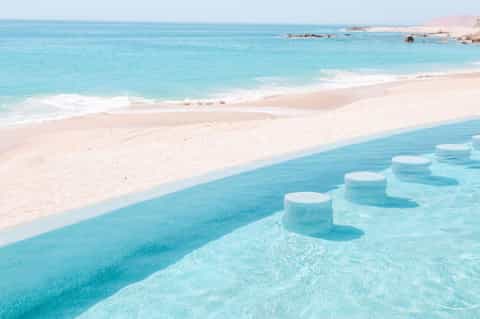 Pristine turquoise lagoon with white sand beach, clear shallow water, and distant rocky coastline