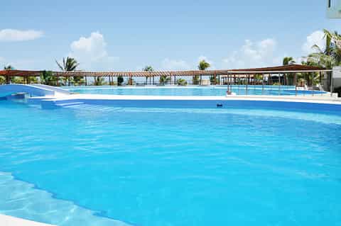 Large bright blue resort swimming pool with palm trees and wooden pergola