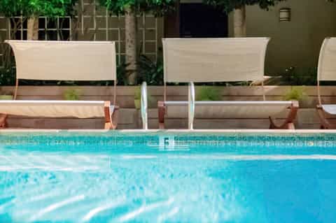 Pool with lounge chairs and cream-colored sun shade panels backed by green garden wall