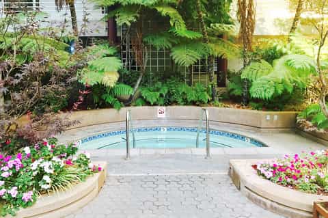 Spa hot tub surrounded by colorful flowers and lush ferns with stepping stone pathway