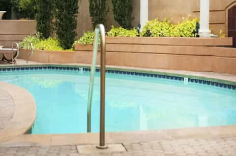 Turquoise swimming pool with wooden privacy fence and desert landscaping at daytime