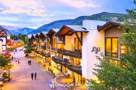Illuminated alpine lodge courtyard at dusk with mountain views and wooden chalets with warm lighting