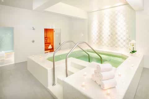 Spa hot tub with green water and rolled white towels, sauna door visible in background