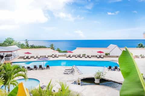 Beachfront resort pool with ocean view, loungers, and pink umbrellas