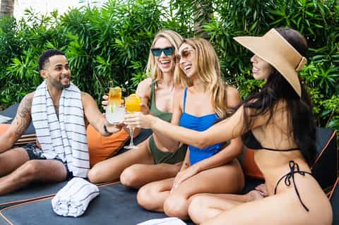 Group of friends enjoying cocktails by pool with greenery backdrop