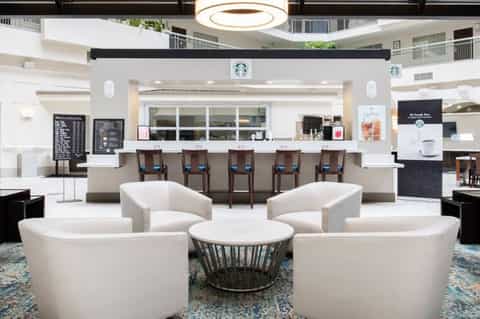 Modern hotel lobby with white curved seating, Starbucks counter, and circular ceiling light