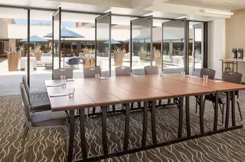 Modern conference room with long wooden table, glass doors opening to terrace with blue umbrellas and mountain views
