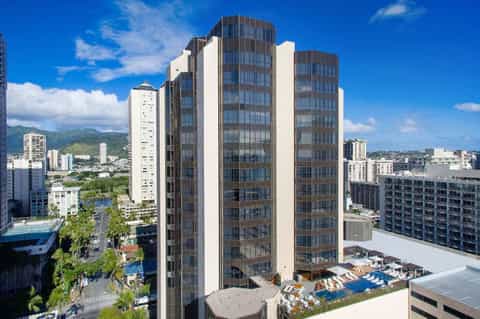Tall residential hotel tower with curved brown and white facade overlooking city with mountains and blue sky