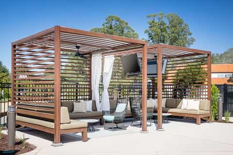 Outdoor wooden pergola lounge with seating, ceiling fan, and slat privacy screens