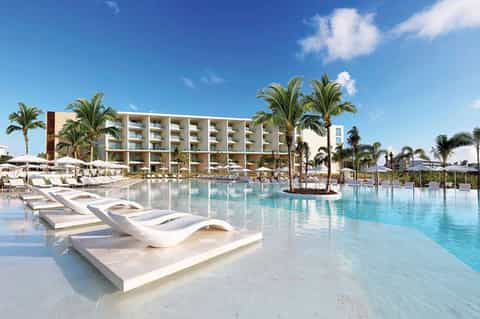 Resort pool area with white loungers, palm trees, and modern beachfront hotel building