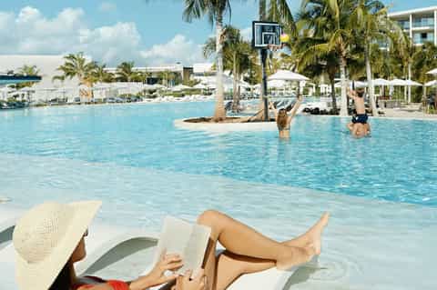 Woman relaxing in shallow lagoon pool with basketball hoop and palm trees at resort
