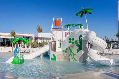 Colorful children's water playground with white slide, water sprays, and tropical palm trees