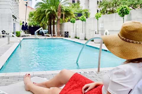 Woman relaxing poolside in urban hotel courtyard with palm trees and modern architecture