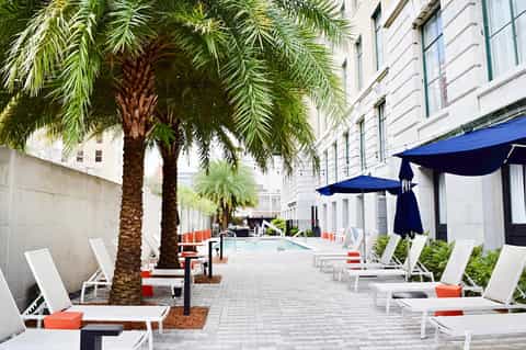 Urban courtyard with lounge chairs, palm trees, blue umbrellas, and modern hotel building architecture
