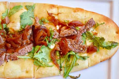 Gourmet sandwich on white plate with meat, caramelized onions, and fresh herbs