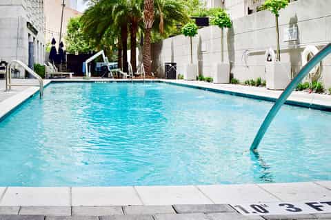 Urban hotel pool surrounded by white buildings, palm trees, and wooden lounge chairs
