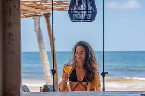 Woman enjoying a cocktail on a beach cabana with palm trees and ocean view