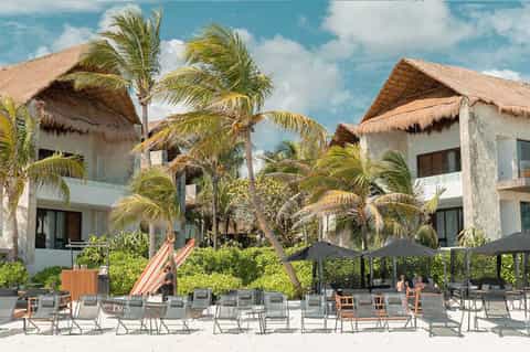 Beachfront resort with thatched-roof villas, palm trees, and beach lounge chairs