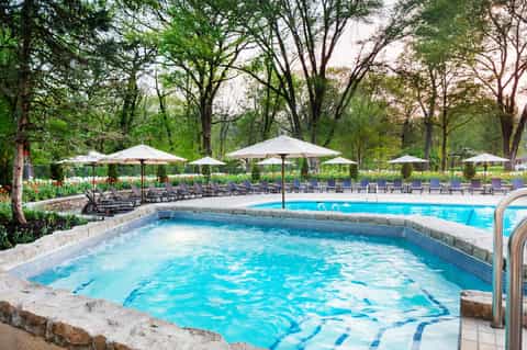 Resort hot tub surrounded by lounge chairs and white umbrellas in a wooded garden setting