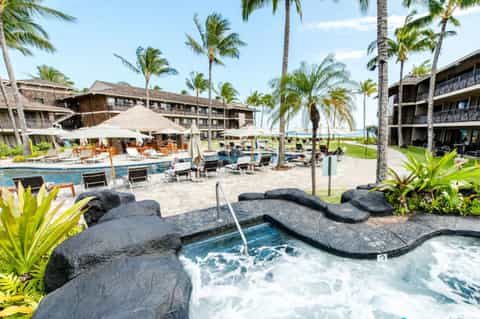 Tropical resort pool area with hot tub, palm trees, lounge chairs, and ocean views