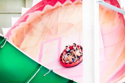Aerial view of family on red inflatable raft under pink and orange parachute