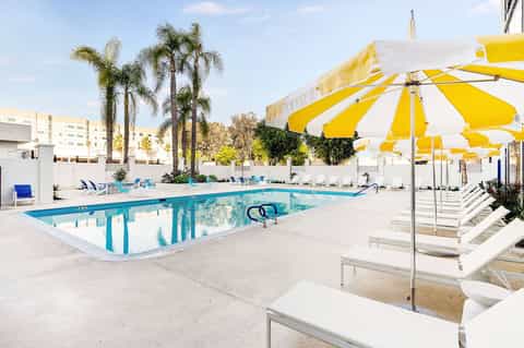 Resort swimming pool with yellow and white umbrellas, lounge chairs, and palm trees under blue sky