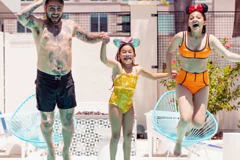 Family of three celebrating in pool wearing Mickey ears and colorful swimwear on rooftop deck
