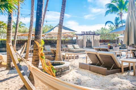 Beach club with hammocks, lounge chairs, palm trees, and shade structures on sandy area