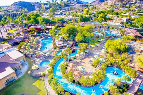 Aerial view of resort with multiple bright blue pools surrounded by palm trees and desert hills