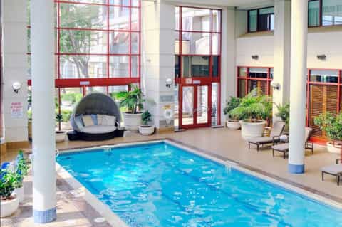 Indoor heated pool with red metal framed windows, lounge seating, bubble chair, and modern architectural design