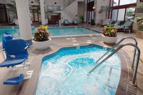Indoor pool area with jacuzzi, white potted plants, lounge chairs, and modern architecture